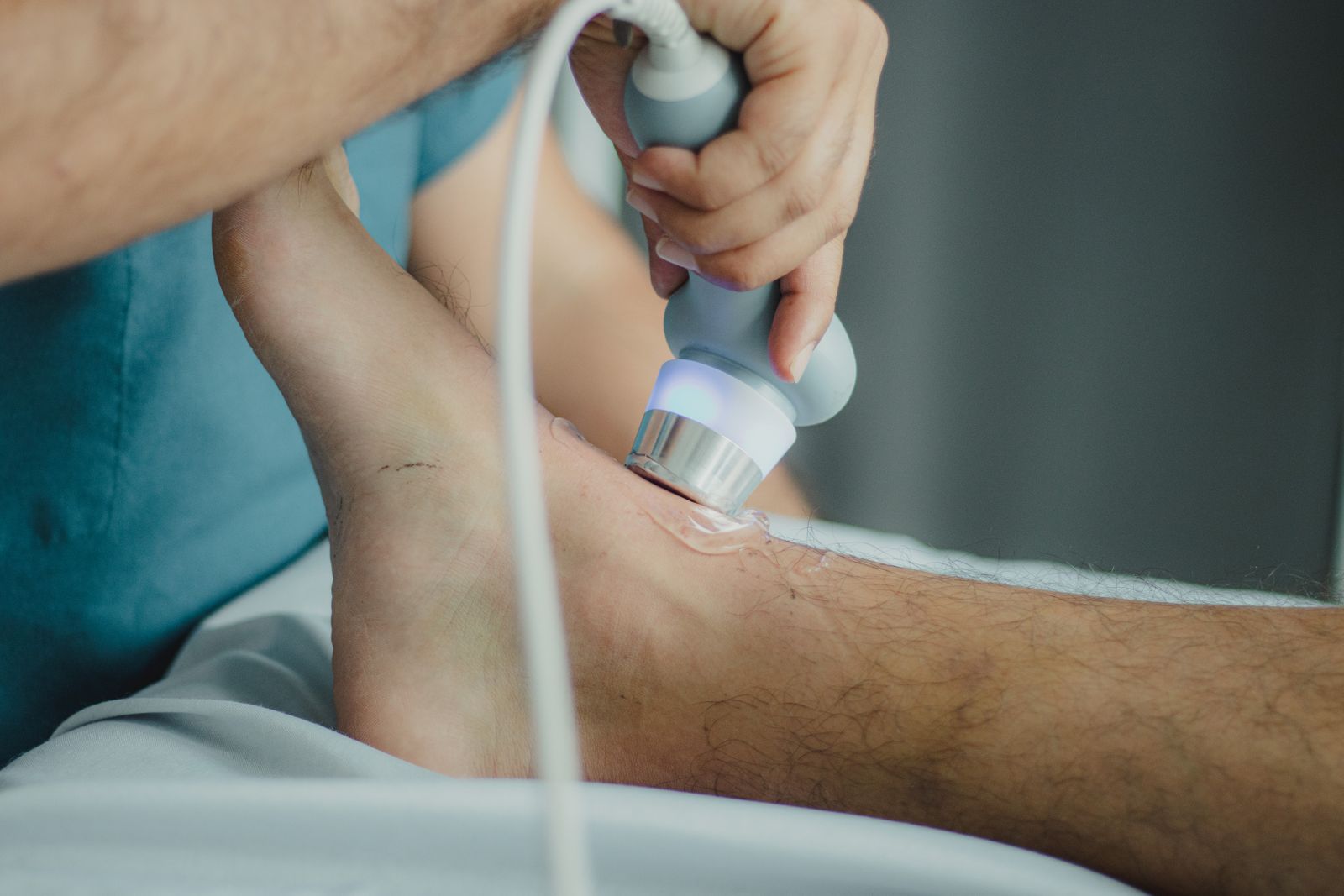 A clinician treating the lower calf and Achilles area of a patient's leg in a clinical setting