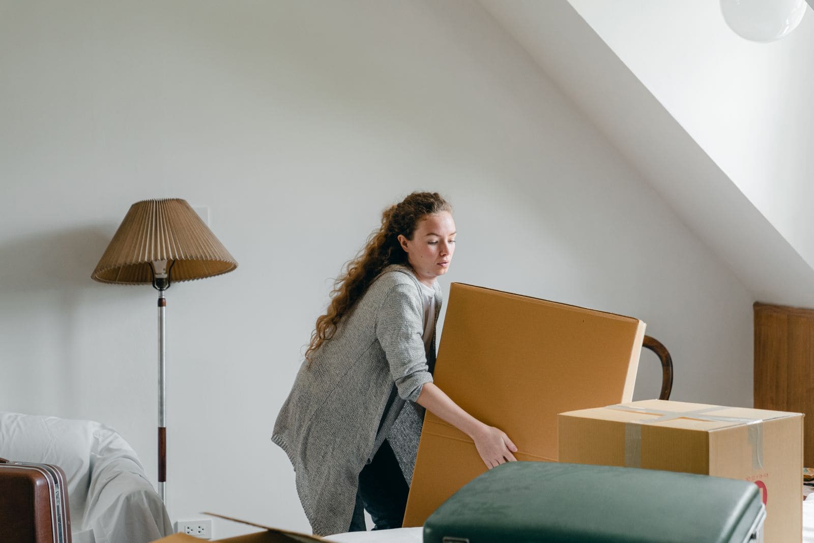 Woman lifting a large cardboard box in a bright attic room during a house move