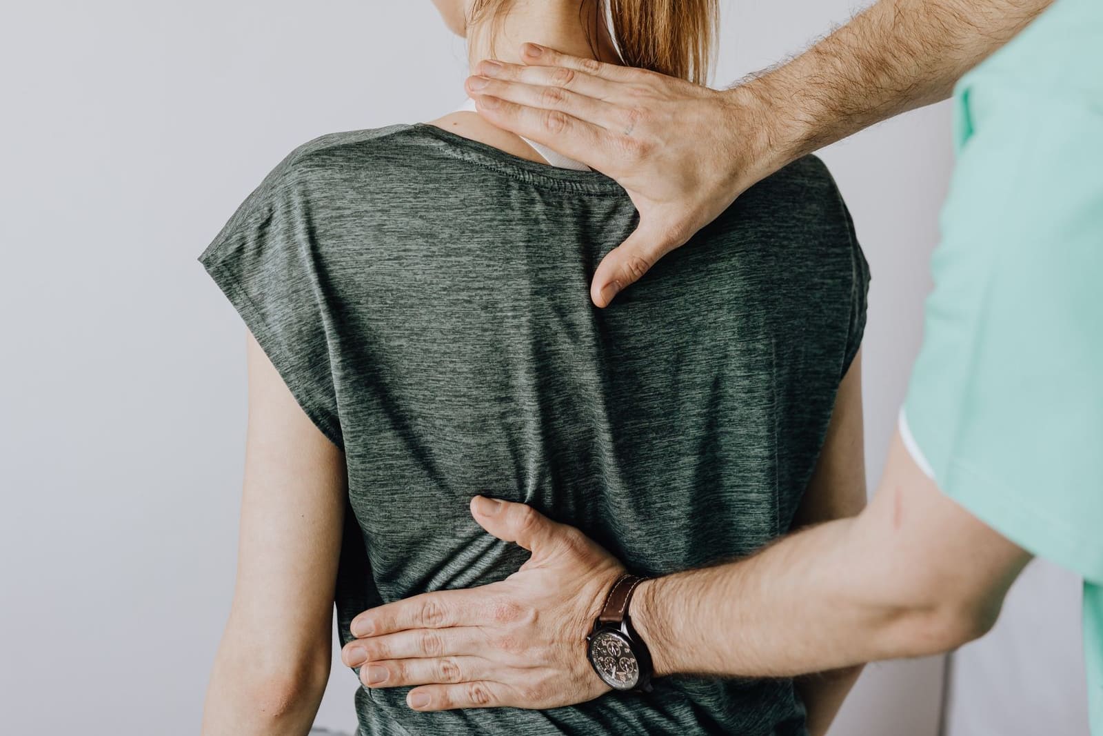 An osteopath with one hand on a seated patient's upper back and one on her lower back during an assessment